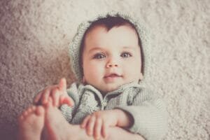 Baby on gray knit hooded clothes lying on carpet